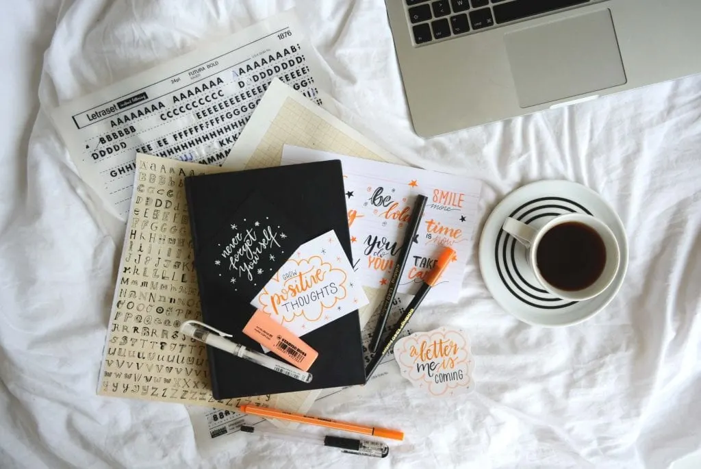 Journal placed on top of a bed. White sheets, wrinkled and cozy, orange pens, white coffee mug with white saucer half full with black coffee. www.everythingabode.com Affiliate Marketing