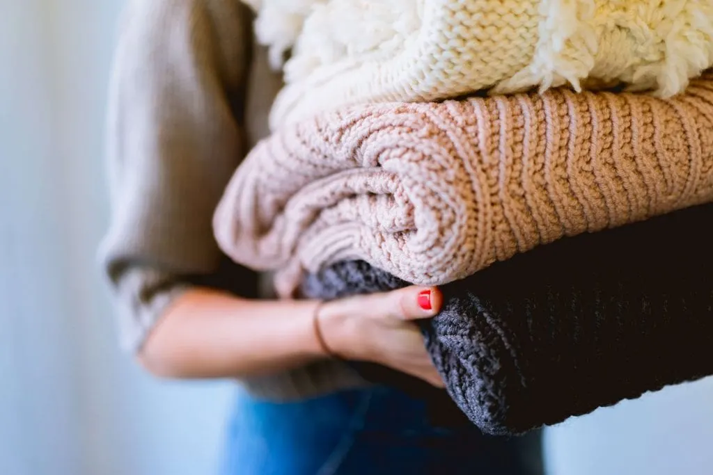 Do smaller laundry loads tip - Girl holding three folded sweaters, pink beige and purple. www.everythingabode.com