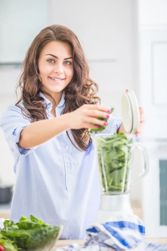 woman making green smoothie in kitchen with blender to detox her body