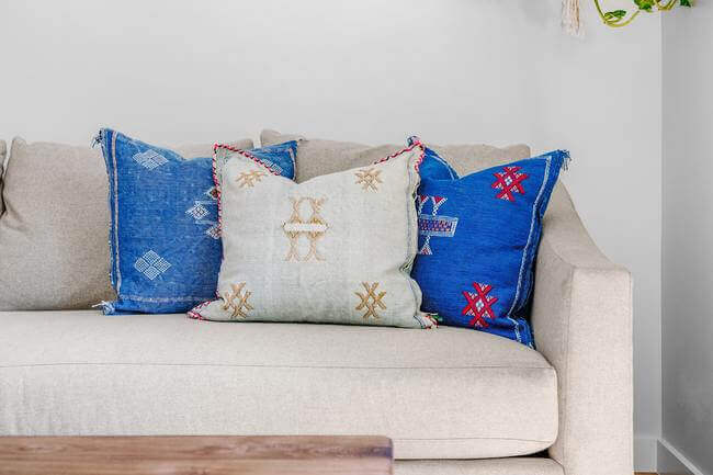 beige sofa in living room with three pillows, two blue and one beige with tan embroidery. Items to declutter in living room