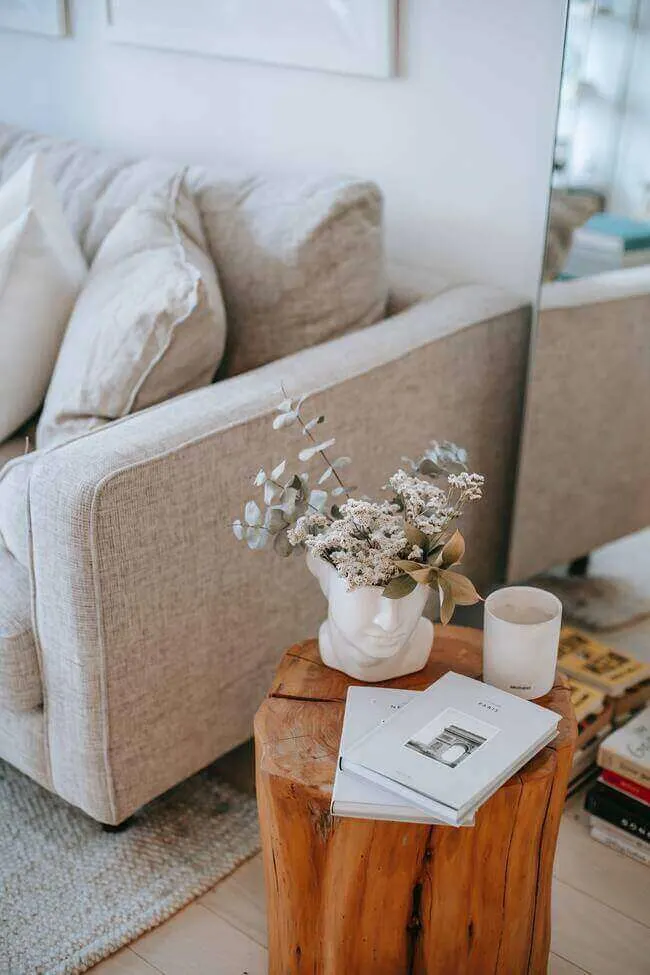 living room items to discard and organize, side table in living room next to grey sofa with a white coffee mug and the side table is a wooden log. Very nice style!