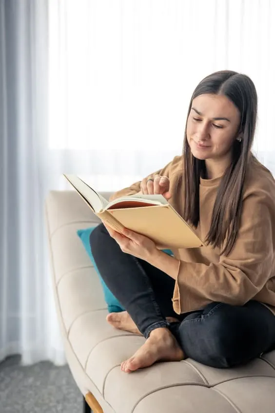 young women reading book on sofa getting motivated