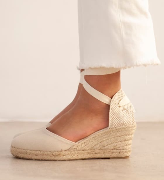 Neutral canvas wedge espadrilles with delicate ankle strap, complemented by frayed white jeans