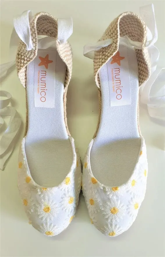 White daisy-embellished espadrille flats with elegant ribbon ties on a light background
