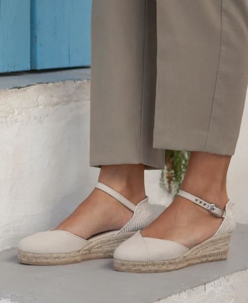 Cream closed-toe espadrille flats with ankle strap on a white and blue backdrop