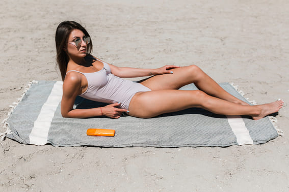 women wearing sunglasses lying on the beach on her designer beach towel on a sunny day