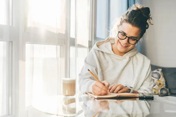 a woman smiling while looking ar her journal because she finished her daily self care journal prompts for personal growth!