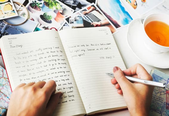 up close look at a woman writing in her diary with journal prompts