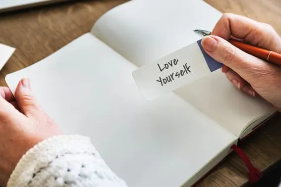 a woman holding a journal prompt in her hand saying, Love Yourself