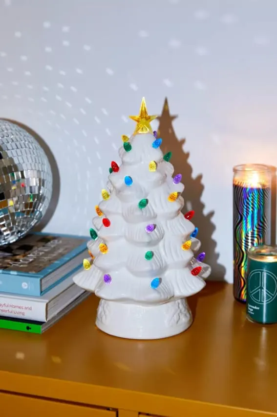 A ceramic Christmas tree with multicolored lights on a book.