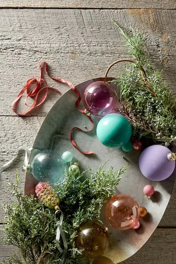 Holiday baubles and greenery on a rustic metal tray.