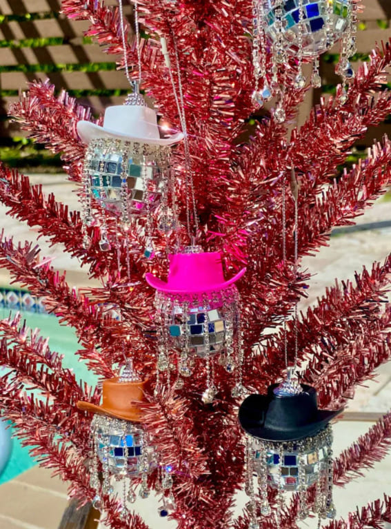 Disco-inspired cowboy hat ornaments on a red tinsel tree.