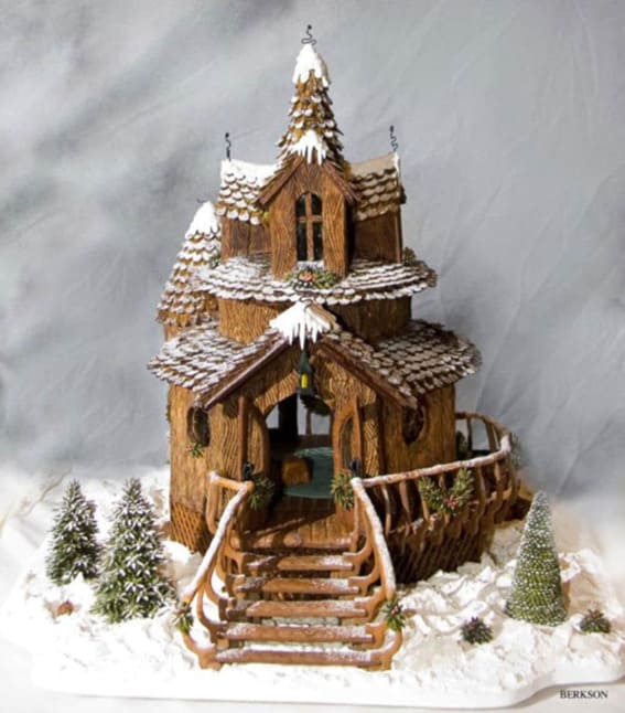 A detailed gingerbread house with almond shingles and pretzel railings in a snowy setting.