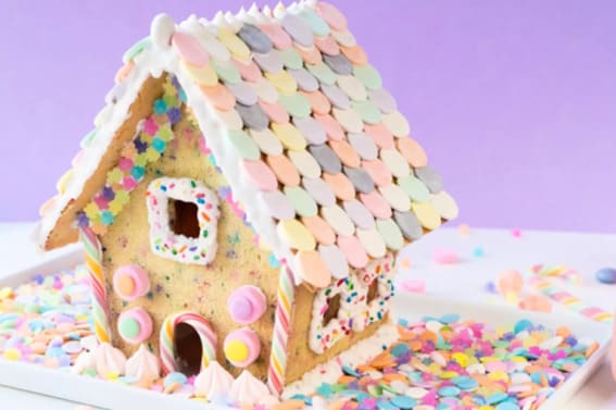 A gingerbread house with a pastel candy roof and whimsical, colorful accents on a confetti-strewn background.