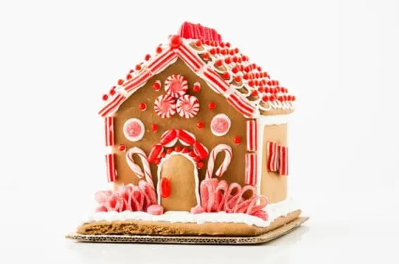 A gingerbread house embellished with peppermint candy and red accents against a white backdrop.