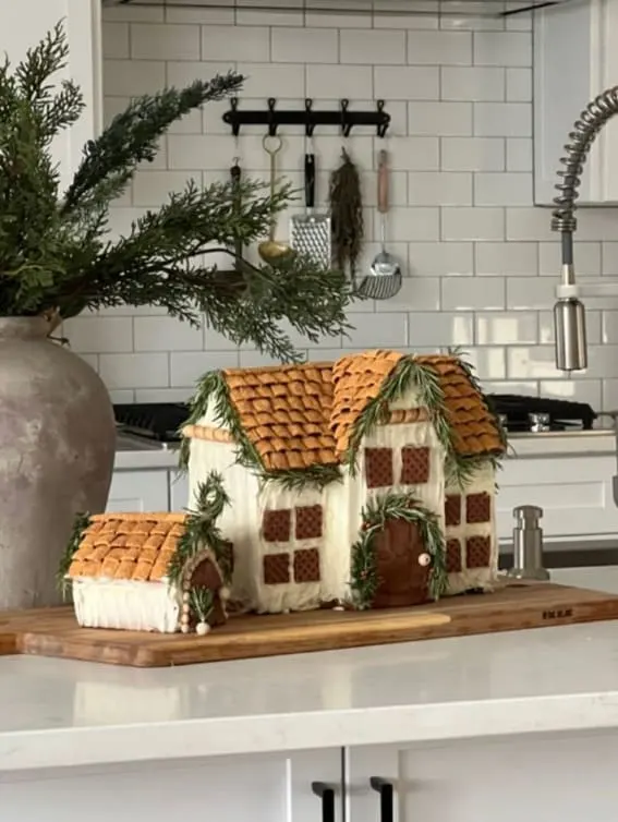 A rustic gingerbread cottage with pretzel stick detailing and graham cracker roofing, set in a modern kitchen.