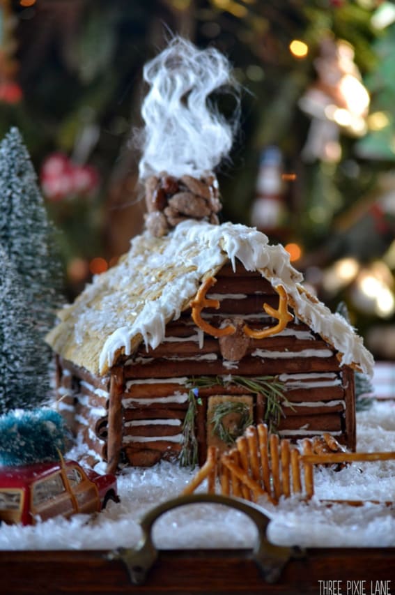 A cozy gingerbread cabin with a smoking chimney and pretzel fencing in a festive setting.