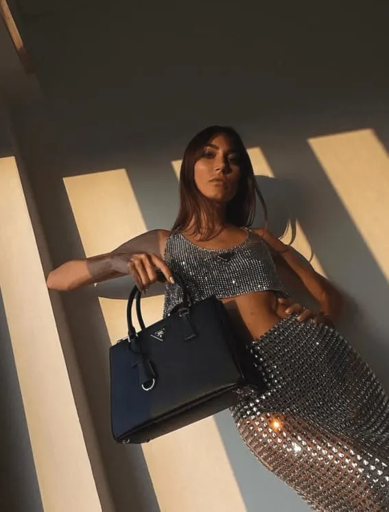 A woman making a bold statement with a metallic silver sequined two-piece, paired with an elegant black handbag.