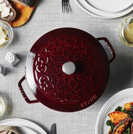 A Staub enameled cast iron French oven with lily embossing on a dinner table.