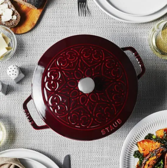 A Staub enameled cast iron French oven with lily embossing on a dinner table.