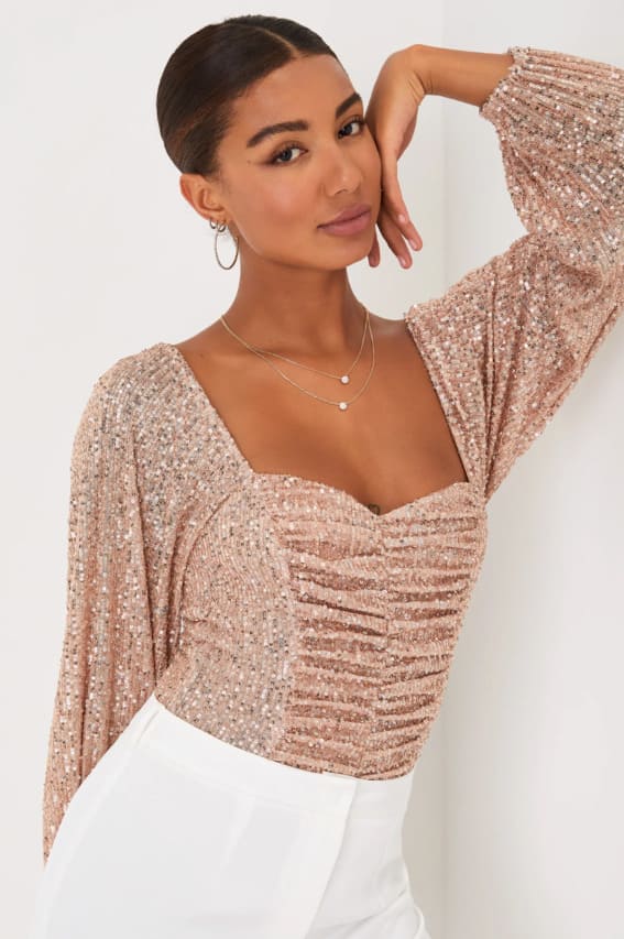 A warm and festive rosy sequined blouse, paired with classic white trousers for a touch of holiday elegance.