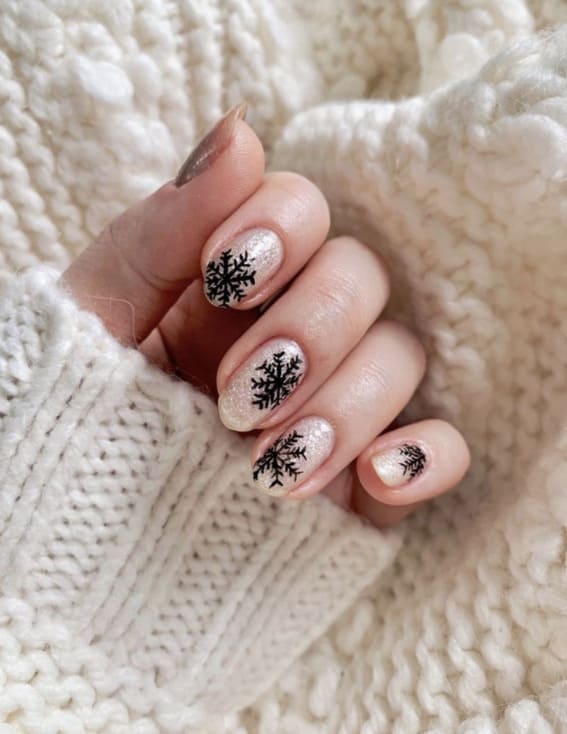 Neutral nails with a shimmering finish and delicate black snowflake designs.