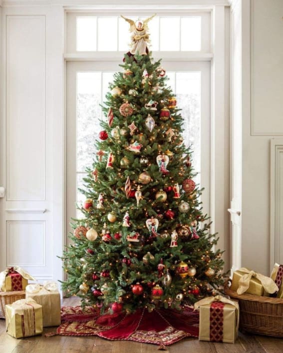 A 6.5-foot Balsam Hill pre-lit BH Balsam Fir premium artificial Christmas tree with clear LED lights, richly decorated and surrounded by gifts.