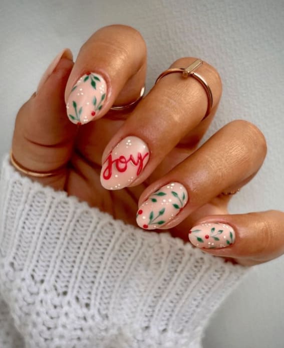 Christmas nails with 'joy' script and holly garland designs on a nude base.