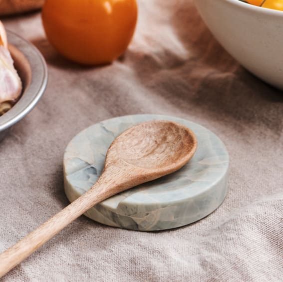 A wooden spoon resting on a blue onyx spoon rest.