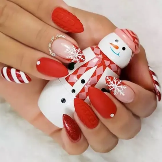 Short nails with festive red and white designs, held alongside a snowman figure