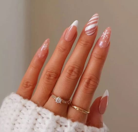 Almond-shaped nails with white French tips, candy cane stripes, and delicate snowflakes.