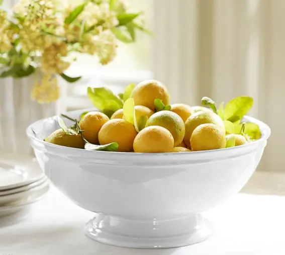 A white stoneware bowl filled with fresh lemons.