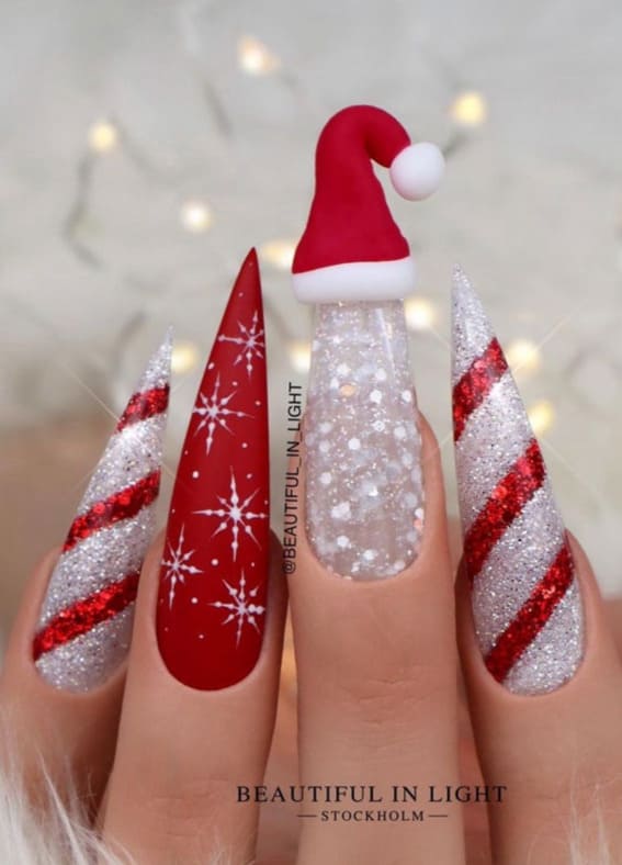 Stiletto nails with red and silver glitter, snowflakes, and a 3D Santa hat design.