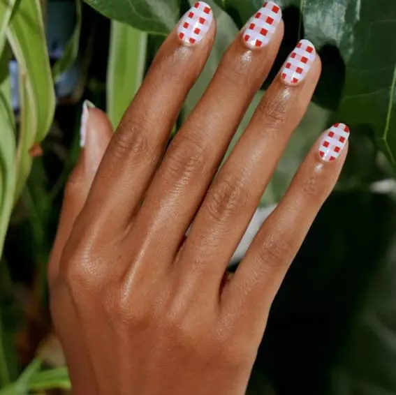 A close-up of a hand showcasing a Christmas-inspired checkerboard nail design.