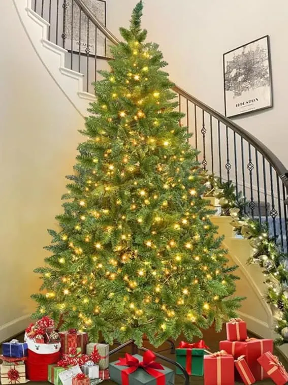 A 6-foot prelit artificial full Christmas tree with 300 warm white lights and realistic 870 branch tips, set beside a staircase with gifts.