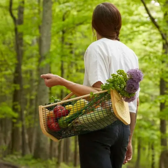 Woman carrying a wooden harvest basket full of fresh produce.
