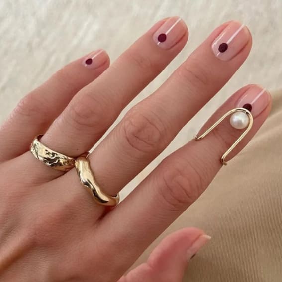 Sheer pink nails with a single burgundy dot on each.