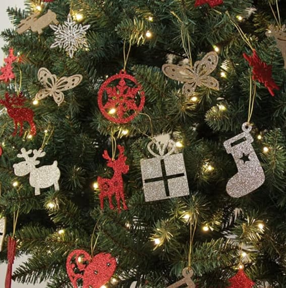 A 6-foot artificial pre-lit Christmas tree with a decoration skirt, 300 warm white LED lights, and adorned with various ornaments, beside a plush teddy bear.