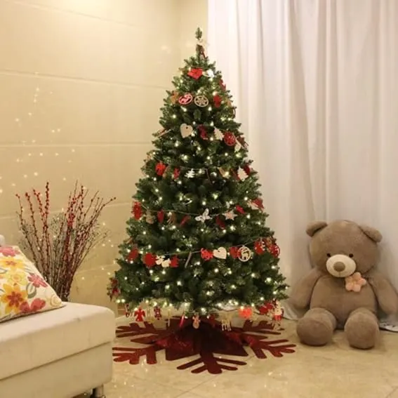 A 6-foot artificial pre-lit Christmas tree with a decoration skirt, 300 warm white LED lights, and adorned with various ornaments, beside a plush teddy bear.
