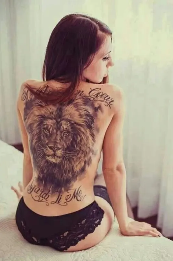 A large and detailed lion tattoo on a person's back with a script