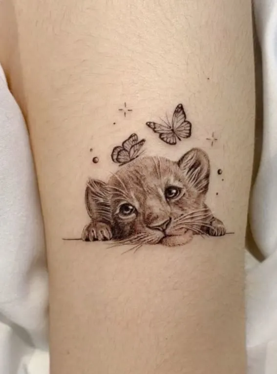 A playful lion cub tattoo with butterflies on a person's arm
