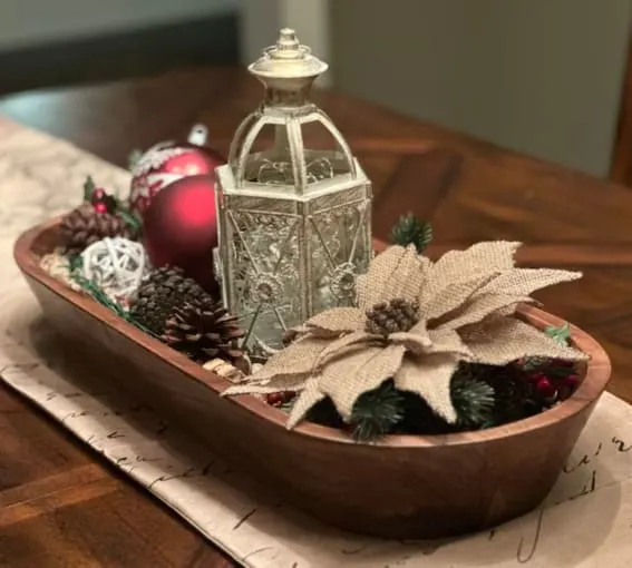 Dough bowl on a dining table filled with holiday ornaments and a lantern