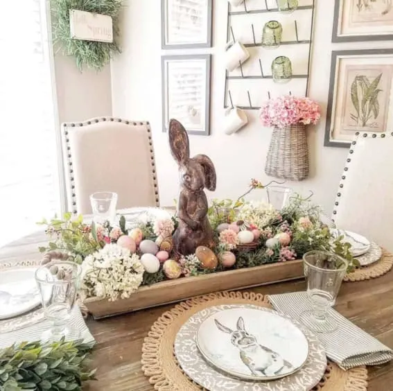A dough bowl on the dining table featuring a chocolate bunny, assorted flowers, and Easter eggs