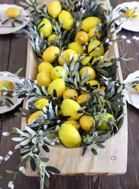 Dough bowl on a wooden table filled with lemons and olive branches