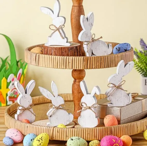 Six rustic wooden bunny signs displayed on a tiered tray among Easter eggs.