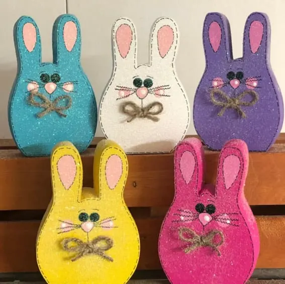 A collection of six glittery wooden bunny decorations in vibrant spring colors.