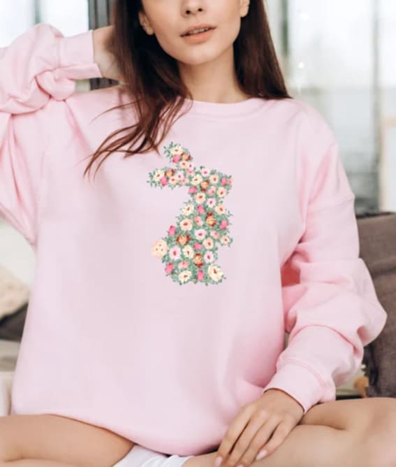 A woman wearing a pastel pink sweatshirt featuring a floral bunny design on it