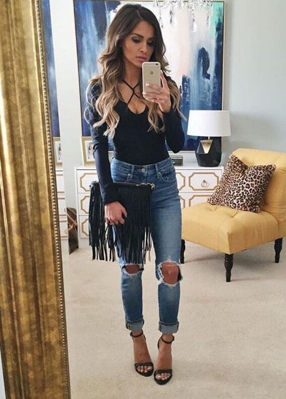 Woman rocking a black leather corset with classic blue jeans and sneakers.