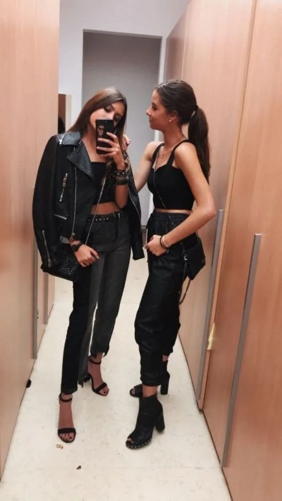 Two friends in chic black outfits posing for a mirror selfie.