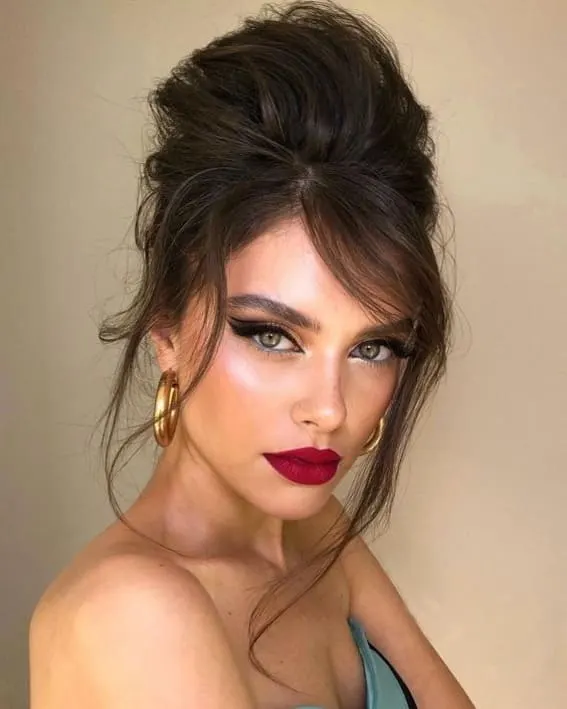 Woman with a voluminous teased updo and striking lip color.